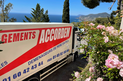 Camion de déménagement Accordem stationné avec vue sur la mer Méditerranée et les collines, entouré de fleurs roses en été